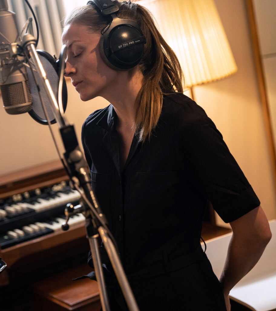 Singer sings with headphones in front of Neumann U47 microphone in recording studio