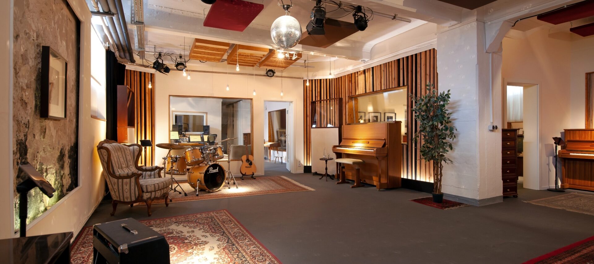 View into large recording studio with piano, drums and other rooms.